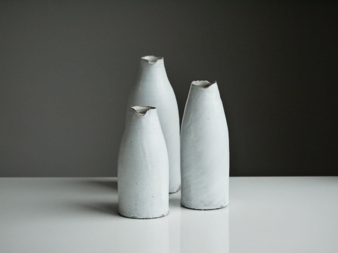 Three white ceramic vases on a shelf